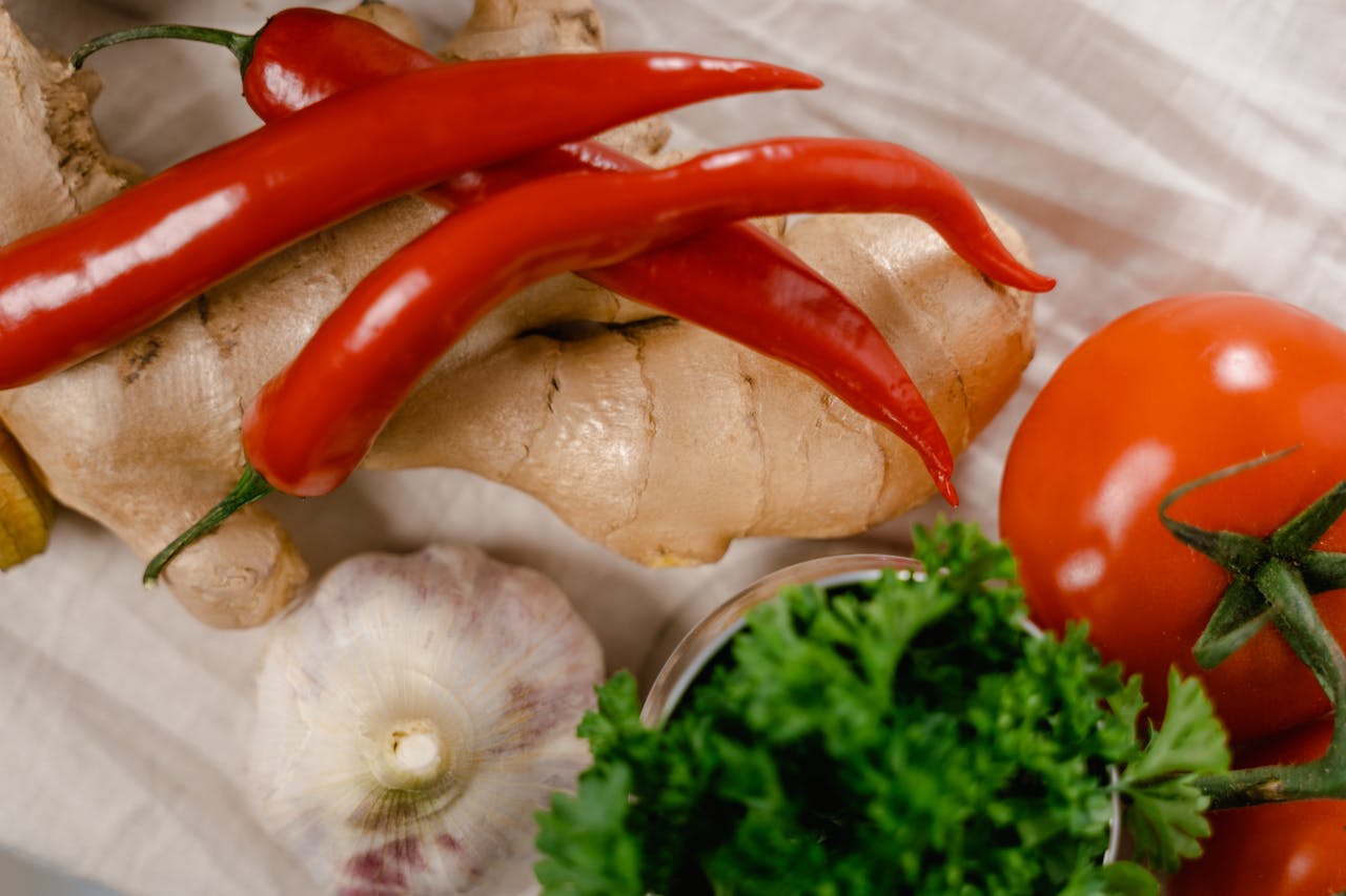 Close-up of fresh ingredients including chili peppers, ginger, and tomatoes on a white fabric surface.